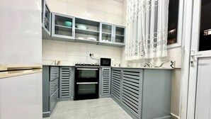 Eine kleine Küche mit grauen Schränken, einer Mikrowelle und einem Fenster mit gemusterten Vorhängen.