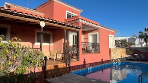 Un edifici de dues plantes amb piscina, un porxo cobert i vistes al mar.