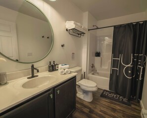 A modern bathroom with a sink, toilet, and shower. There are toiletries on the sink and a towel rack above the toilet. - Hunter House (Livingston Manor)