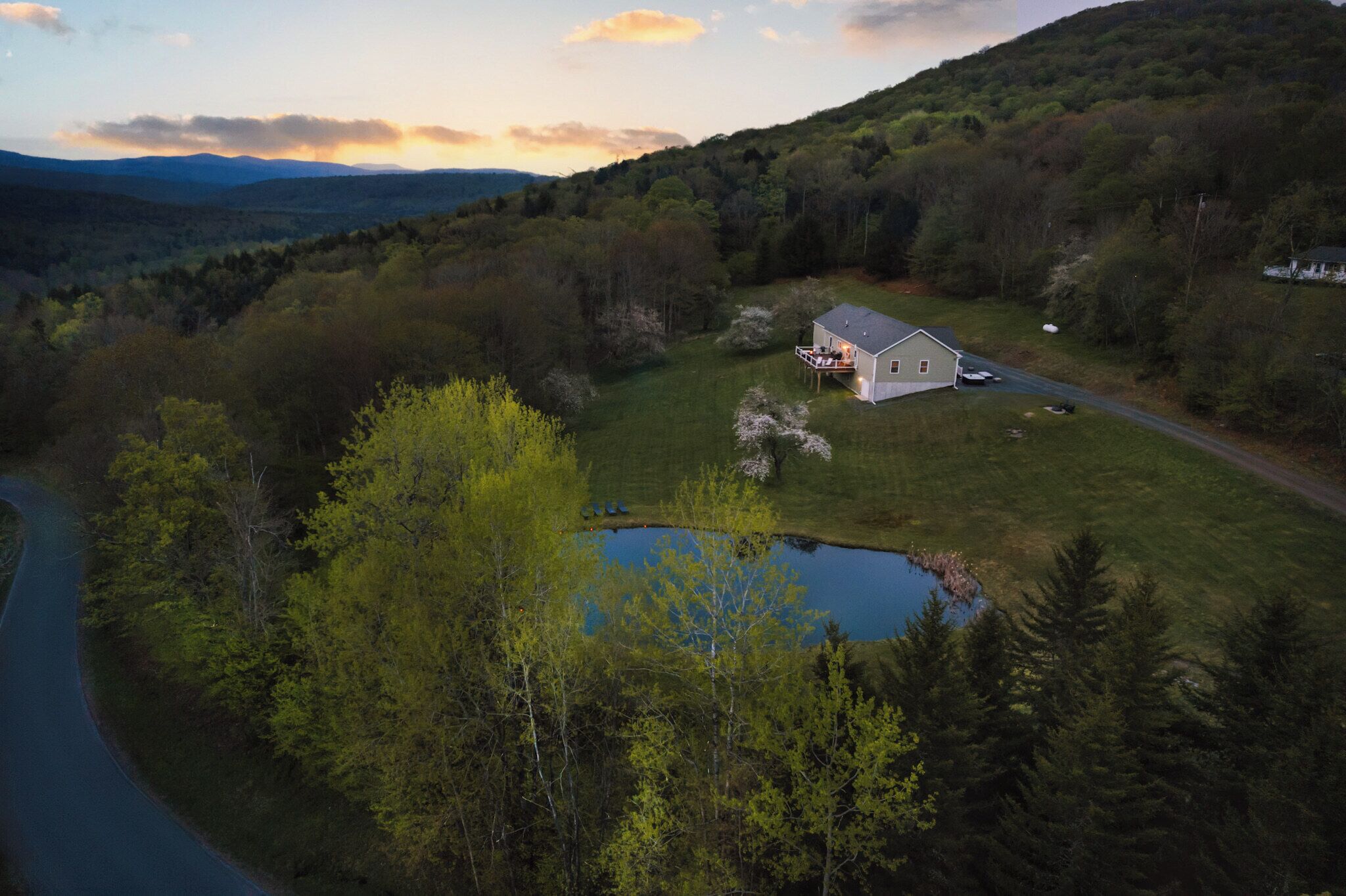 A house with a large deck and a pond in a forested area.