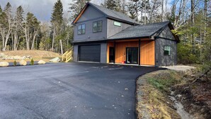 Kaksikerroksinen talo, jossa on autotalli, ja sen ympärillä on metsä.
