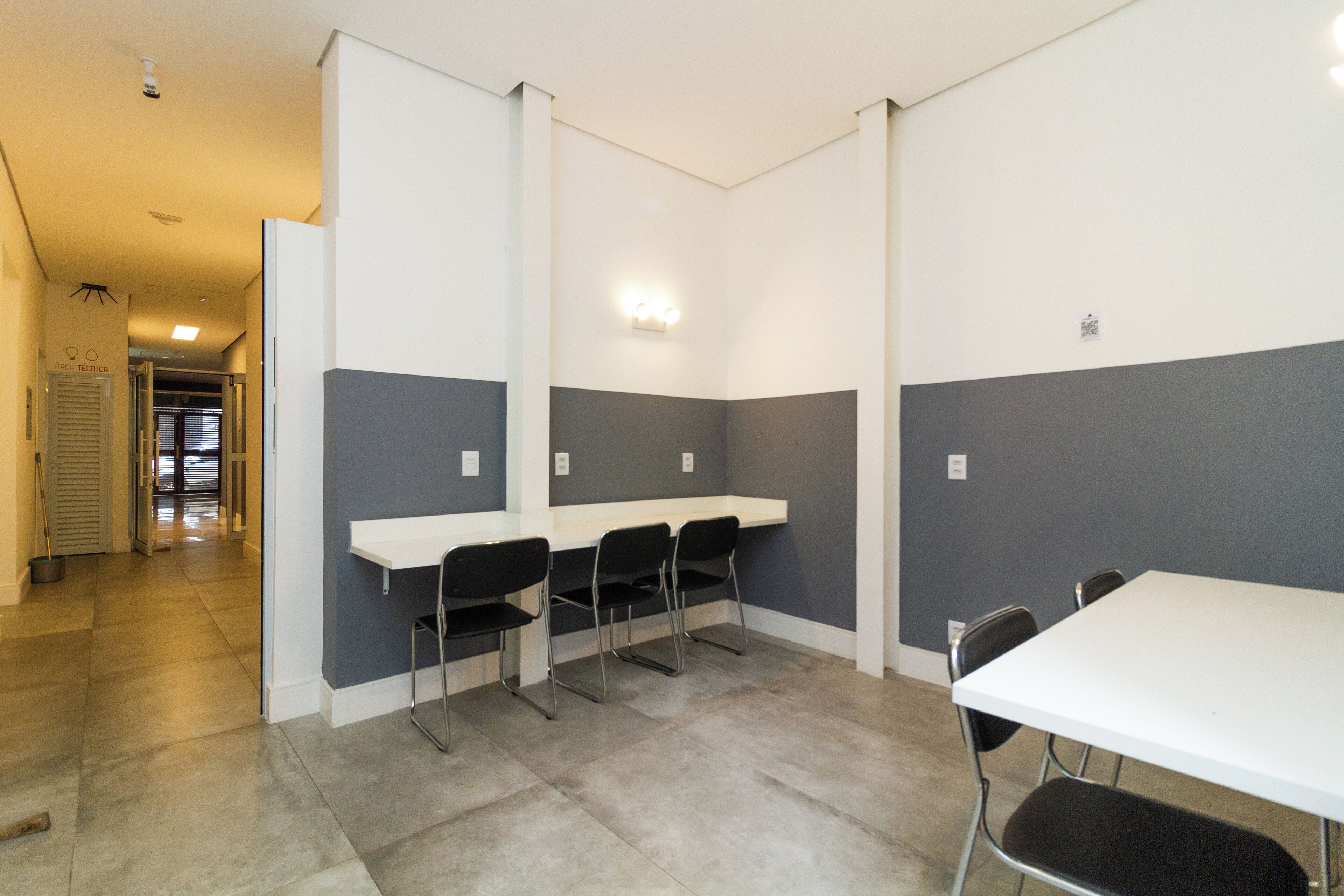 A conference room with a white table and four chairs, grey walls, and a ceiling light.