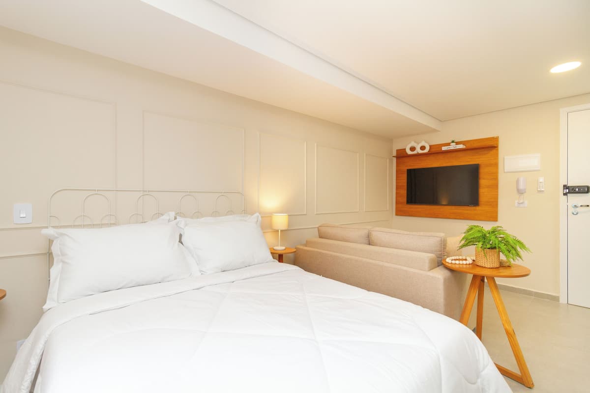 Une chambre d’hôtel avec un lit, un canapé, un téléviseur fixé au mur et une petite table sur laquelle est posée une plante.