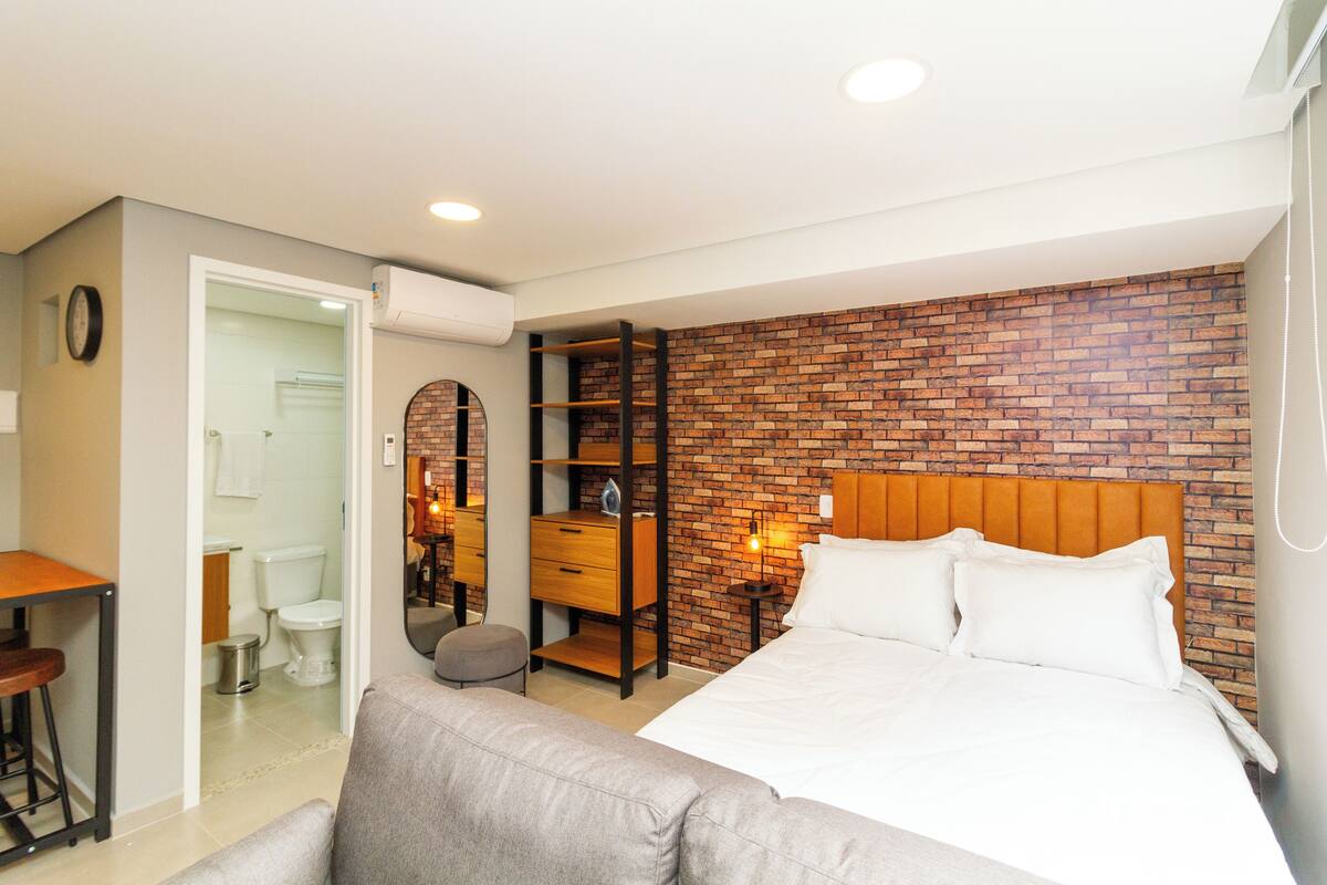 Une chambre moderne avec une tête de lit ornée d’un motif en briques, un grand lit, un bureau avec une chaise et un miroir.