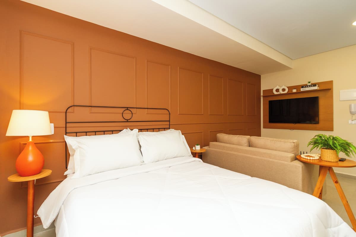 Une chambre d’hôtel comprenant un lit, une table de chevet avec une lampe, un canapé, un téléviseur et un panneau fixé au mur.