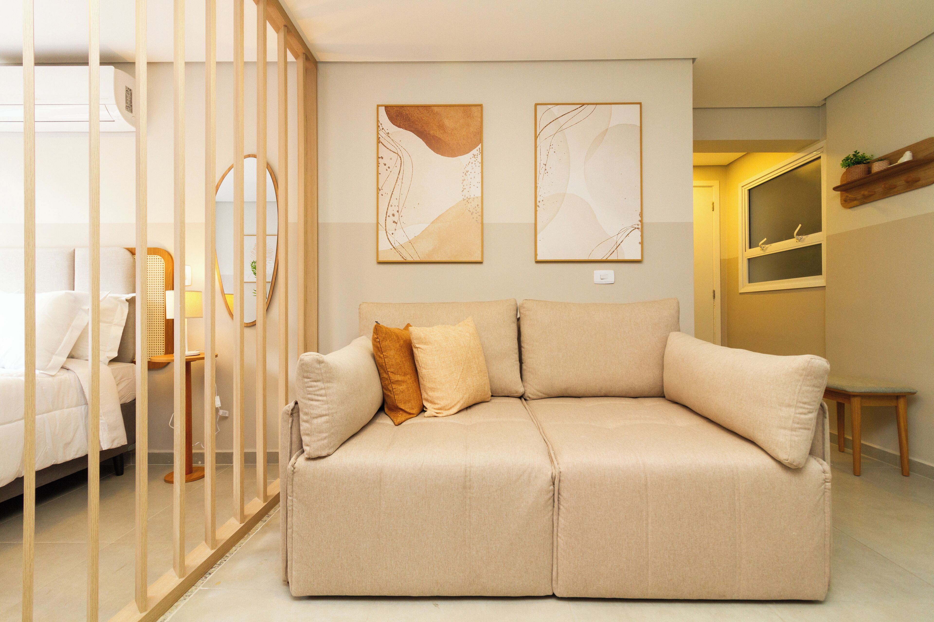 A modern living room with a beige sofa, a wooden partition, and abstract wall art.