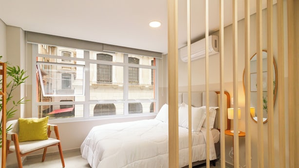 Una camera da letto con una grande finestra, un letto, una sedia e un comodino.