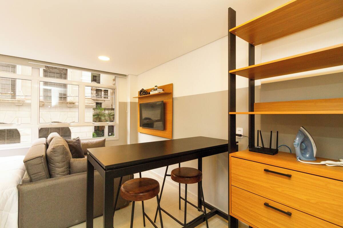 Un espace de vie compact comprenant un canapé, une petite table à manger et un meuble en bois sur lequel est posée une télévision.