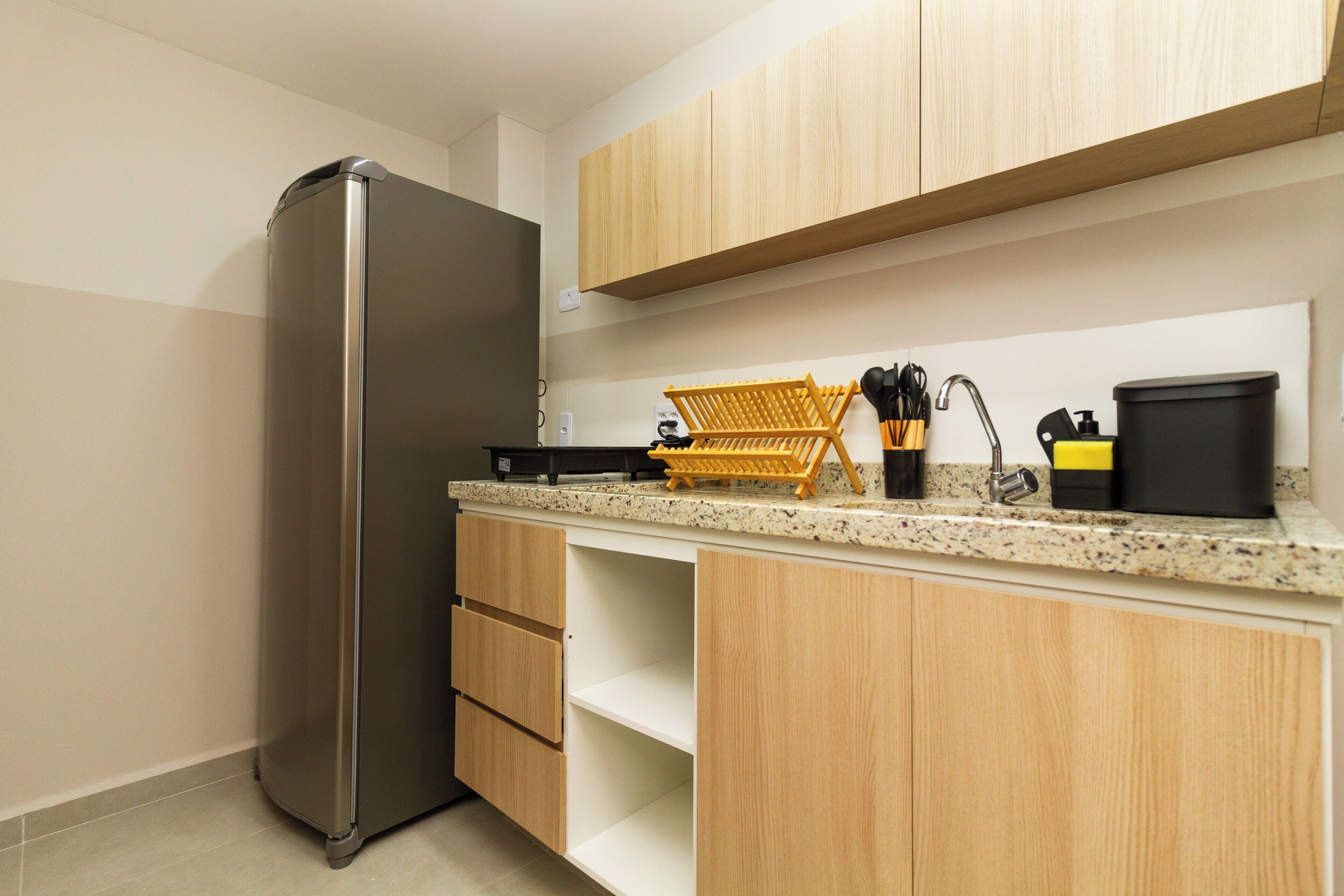 A modern kitchen with a stainless steel refrigerator, wooden cabinets, a granite countertop, and a coffee maker.