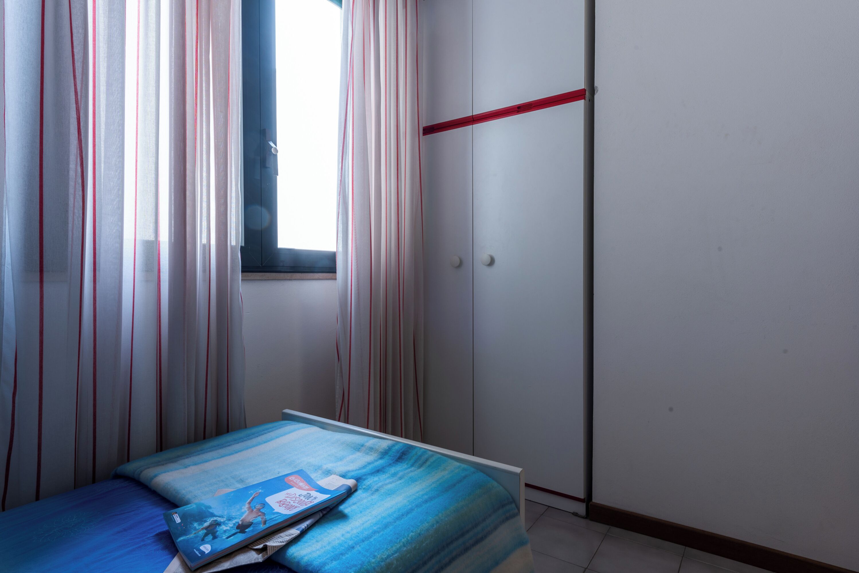 Une chambre à coucher avec un lit, une fenêtre, des rideaux, une armoire et une ligne rouge sur le mur.