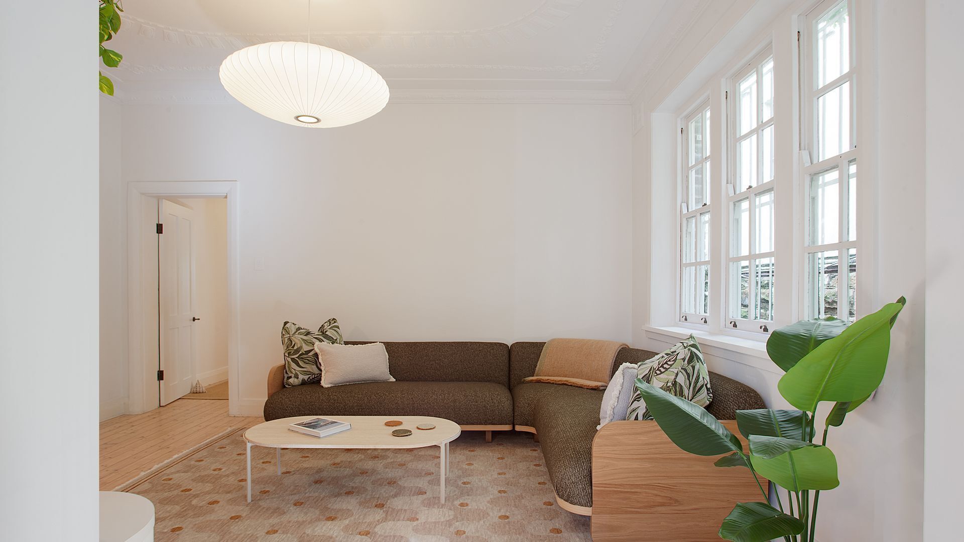 En stue med en brun sofa, et hvidt sofabord og et stort vindue med mange ruder.