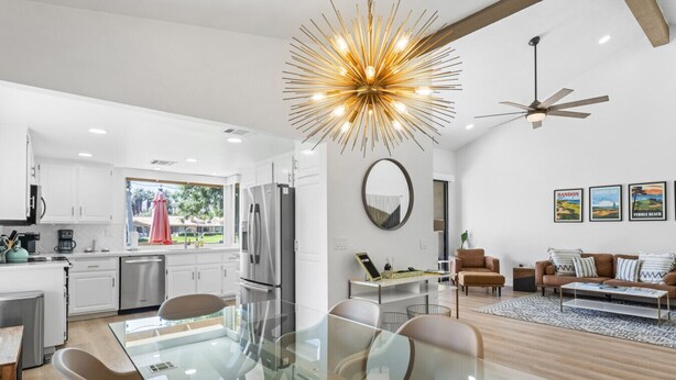A modern kitchen with white cabinets, a stainless steel refrigerator, and a dining area with a glass table and chairs. - The Palmer! Monterey Country Club, Hole 6, Resort Amenities! Golf cart included! (Palm Desert)