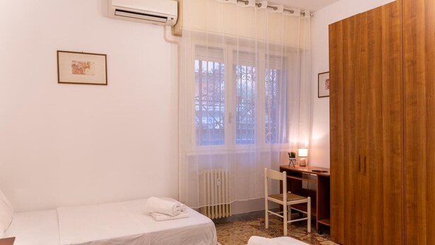 A hotel room with two beds, a desk, a chair, a radiator, and a wooden wardrobe. - Charming studio in  Roma with AC, WiFi, WASHING MACHINE for upto 3 person. (Roma)