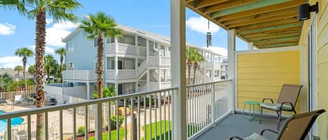 A balcony with a view of a multi-story building, a pool, and palm trees.