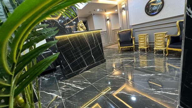 Un vestíbulo con mostrador de recepción de mármol negro, sillas con marco dorado y un diseño de techo moderno.