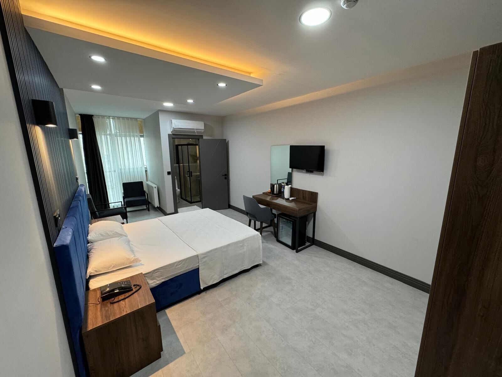 Une chambre d’hôtel moderne équipée d’un lit, d’un bureau, d’une chaise, d’une télévision et d’une salle de bain avec douche et toilettes.