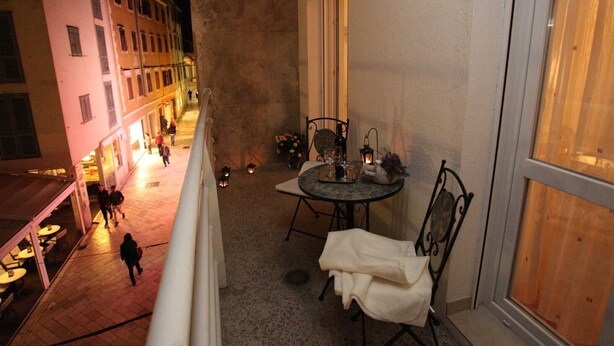 Ein Balkon mit Tisch für zwei Personen, Blick auf eine Straße mit Gebäuden und Passanten.