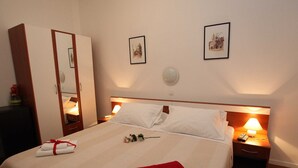 Ein ordentlich bezogenes Bett mit weißer und roter Bettwäsche, ein Nachttisch mit Lampe sowie ein Kleiderschrank.