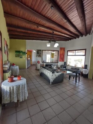 A spacious living area with a high wooden ceiling, a grey sofa, a coffee table, and a small round table with a floral tablecloth. - Hotel Boutique Altos de Amaicha (Amaicha Del Valle)