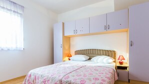 Ein Schlafzimmer mit einem Bett, zwei Nachttischen, einem fensterbepflanzten Fenster und einem Kleiderschrank.