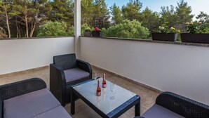 Ein überdachter Außenbereich mit Korbmöbeln und einem Tisch, mit Blick auf einen Garten mit Topfpflanzen und Bäumen.