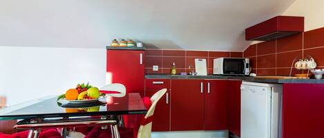 Una cocina moderna con armarios rojos, un lavavajillas blanco y una mesa de comedor de cristal con cojines rojos.