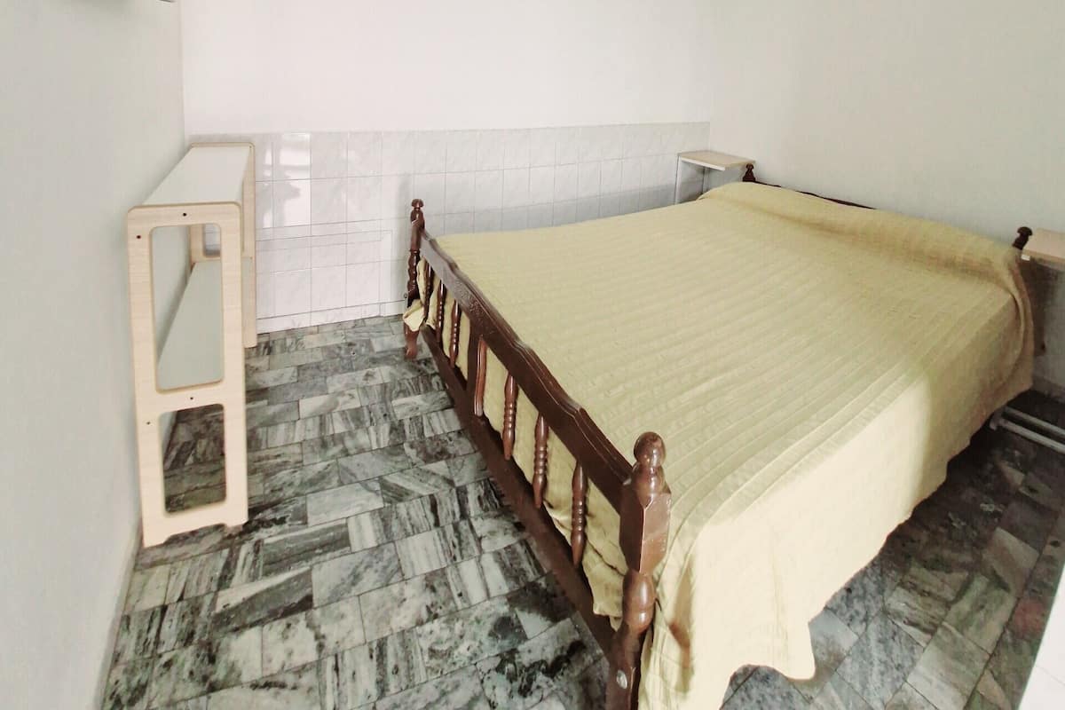 Un dormitorio con una cama, una mesita de noche de madera, un ventilador de techo y un televisor montado en la pared.