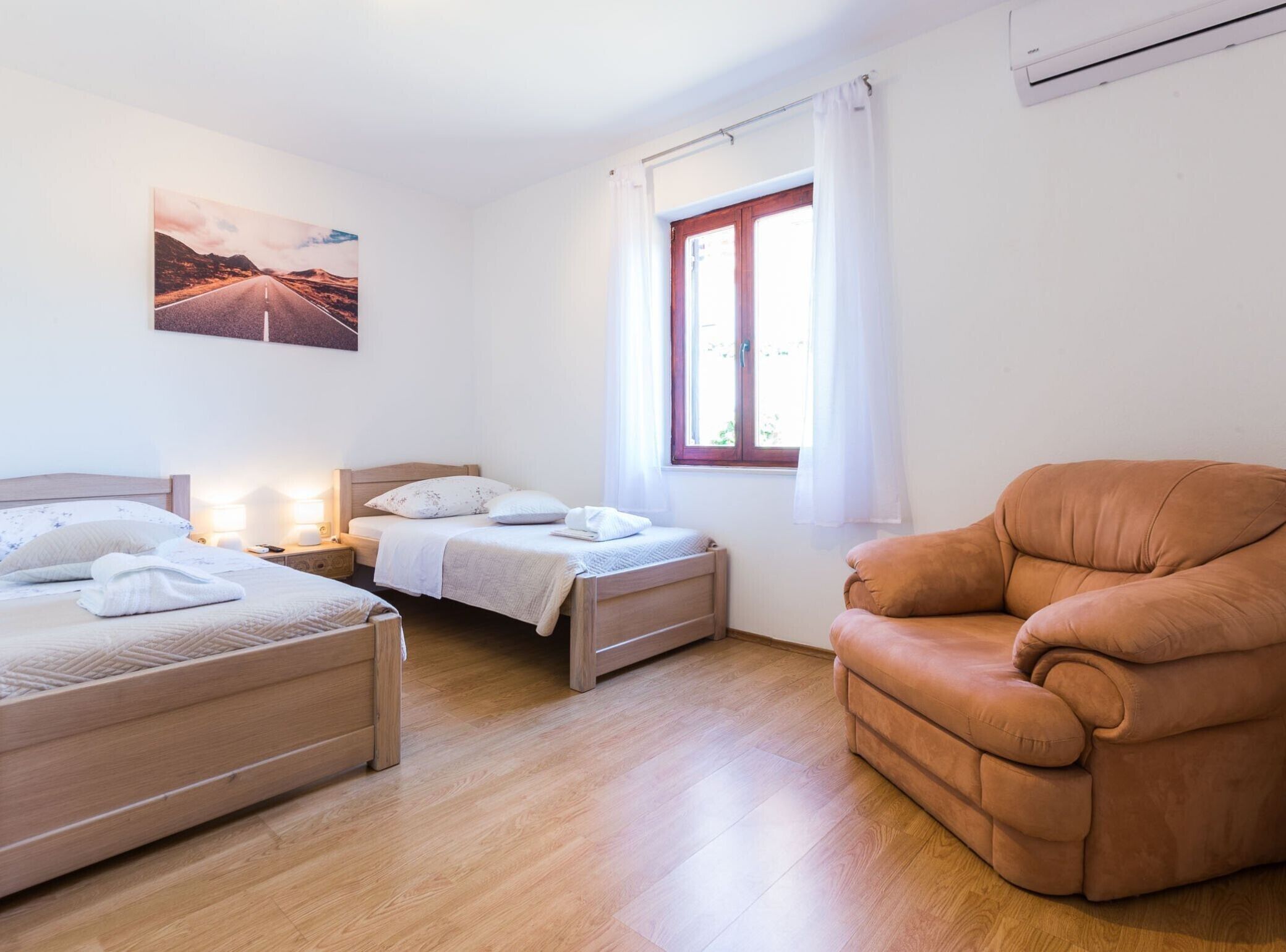 Een slaapkamer met twee bedden, een houten vloer, een raam met gordijnen en een bruine fauteuil.