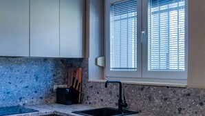Eine Küche mit Granit-Arbeitsplatten, einem schwarzen Spülbecken, Holzschränken und einem Fenster mit Jalousien.