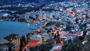 A coastal cityscape with a mix of residential and commercial buildings, a marina, and mountains in the background.