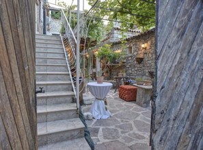 Eine Steintreppe führt zu einem Innenhof mit einem runden Tisch und Pouf, umgeben von Topfpflanzen und Steinmauern.