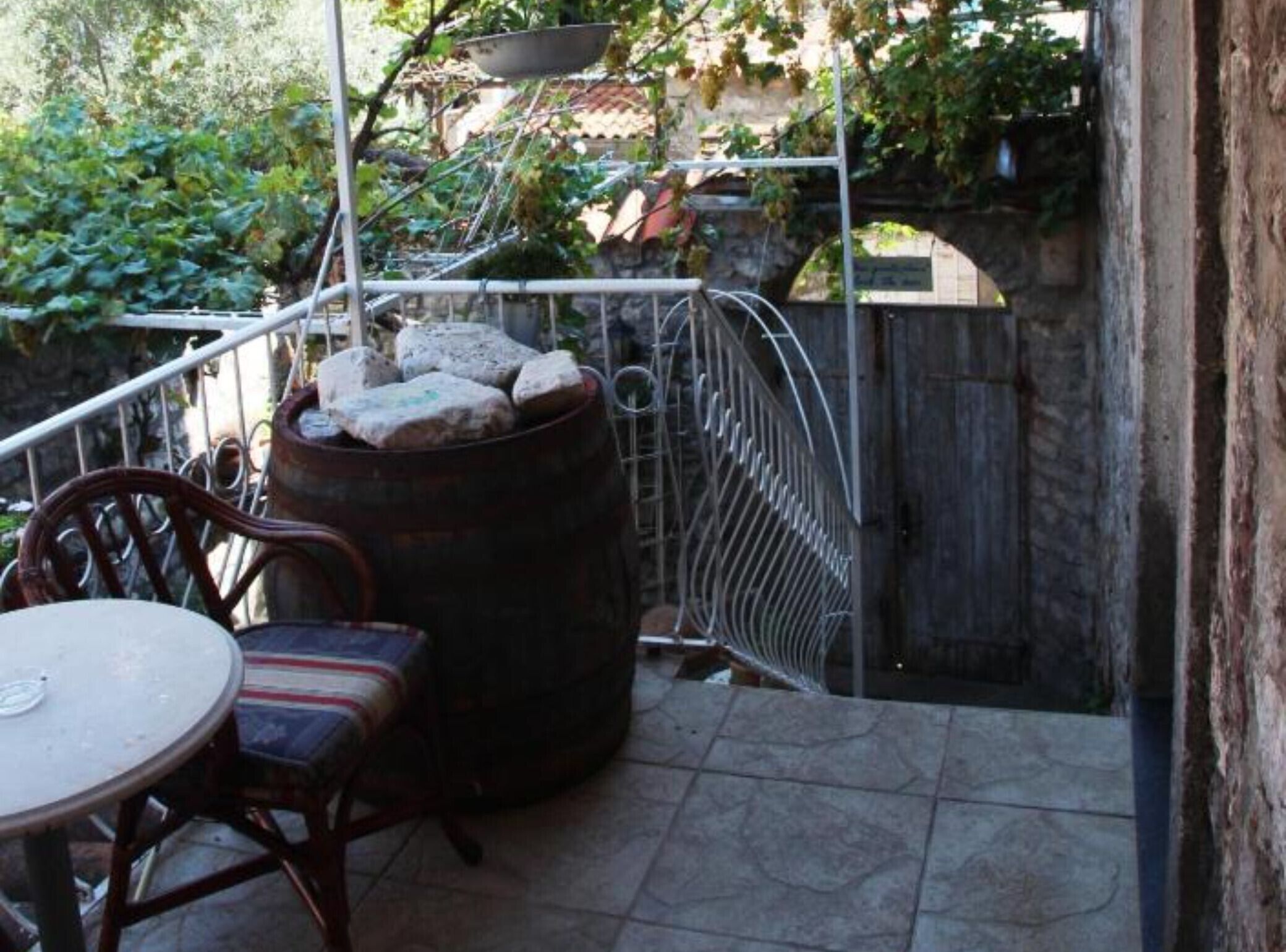 A patio with a round table and chairs, a metal chair, a large barrel, and a metal grill.
