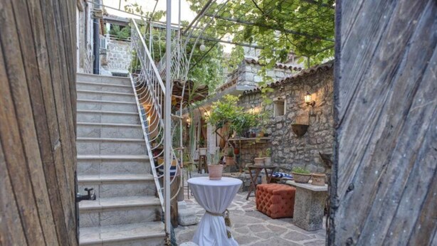 A stone staircase leading to a courtyard with a round table and ottoman, surrounded by potted plants and stone walls. - Quaint & Affordable Stay in Budva Traditional Stone House - Standard Double Room 3 (Budva)