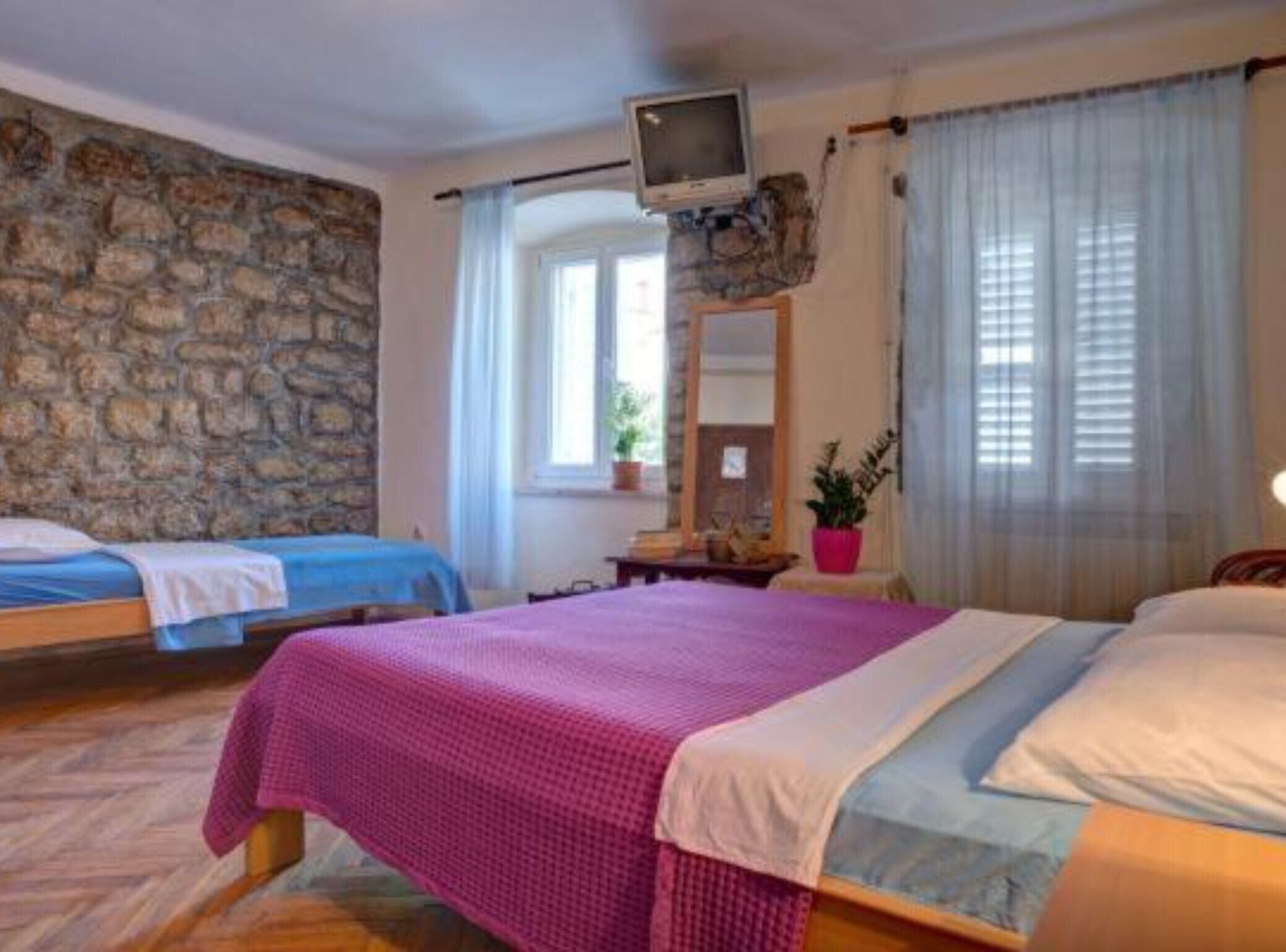 Una camera da letto con due letti, una parete in pietra, un televisore e una finestra con tende.