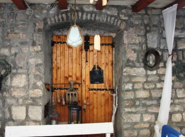 Un mur en pierre avec une porte en bois, un luminaire suspendu et une petite table avec une chaise.