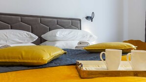 Une chambre d’hôtel avec un lit, des oreillers, un plateau avec une tasse et une lampe fixée au mur.