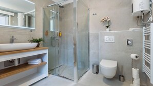 Une salle de bain moderne avec une douche à parois de verre, un lavabo blanc doté d’un plan de toilette en bois, des toilettes et un porte-serviettes.