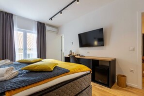Una habitación de hotel moderna con cama, escritorio, televisor y ventana con cortinas.