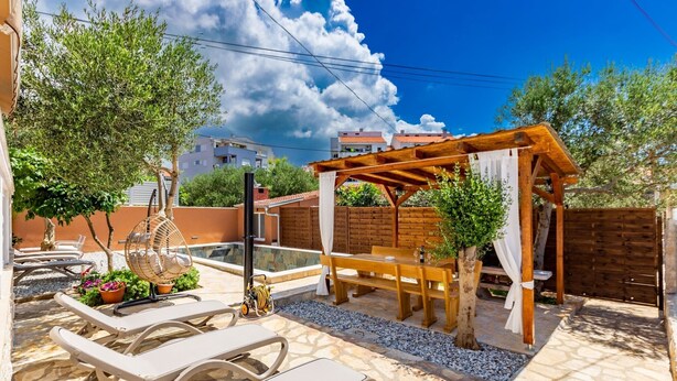 Un patio con mobiliario exterior, una pérgola de madera y un pequeño jardín.