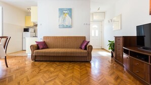 Una sala de estar con un sofá, suelo de madera en espiga, un televisor y un cuadro en la pared.