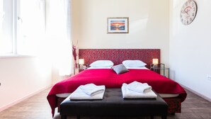 A hotel room with a large bed, two bedside tables with lamps, a clock on the wall, and a painting above the bed.