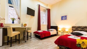 Habitación de hotel con escritorio, dos camas, televisión y ventana con cortinas.