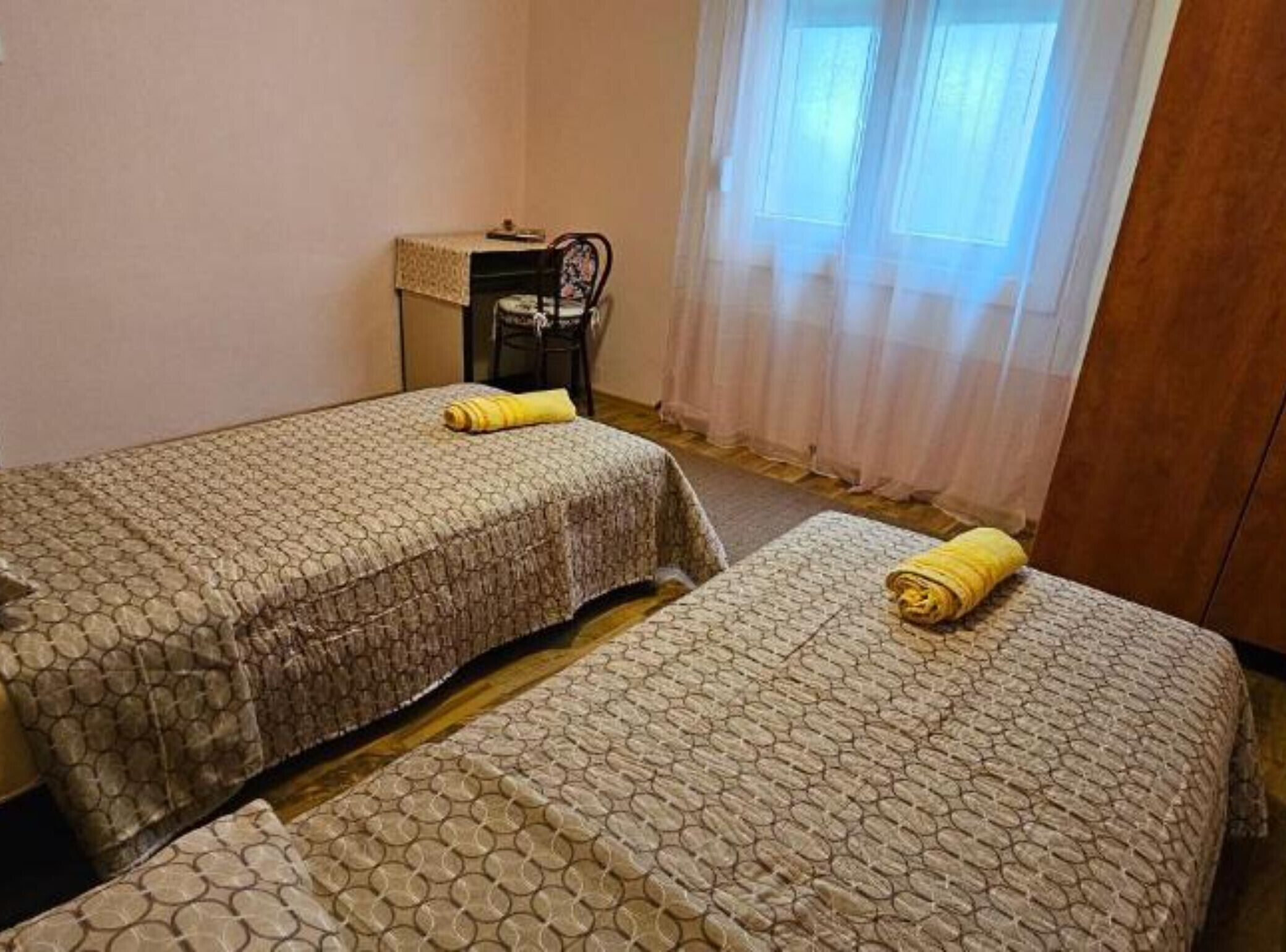 Quarto com duas camas, uma mesa pequena e uma cadeira.