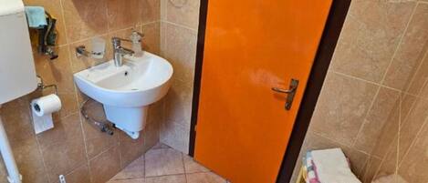 Baño con lavamanos blanco, inodoro y puerta naranja.