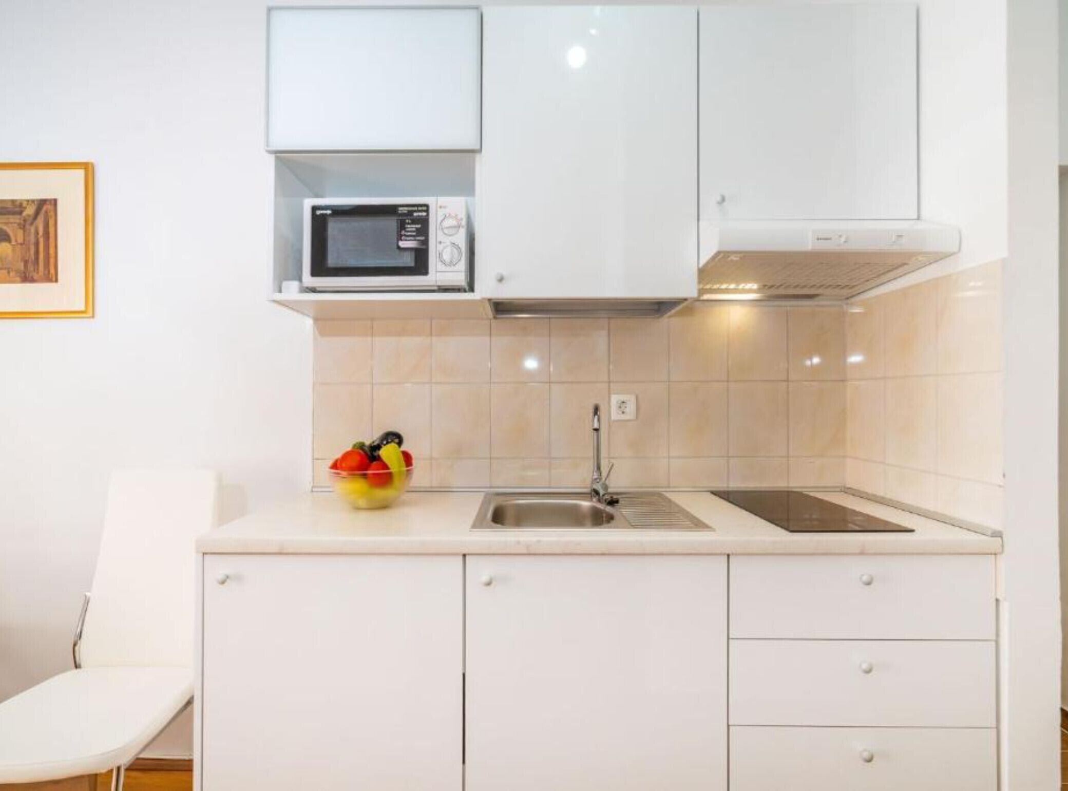 Een moderne keuken met witte kastjes, een magnetron, een spoelbak en een schaal fruit op het aanrecht.