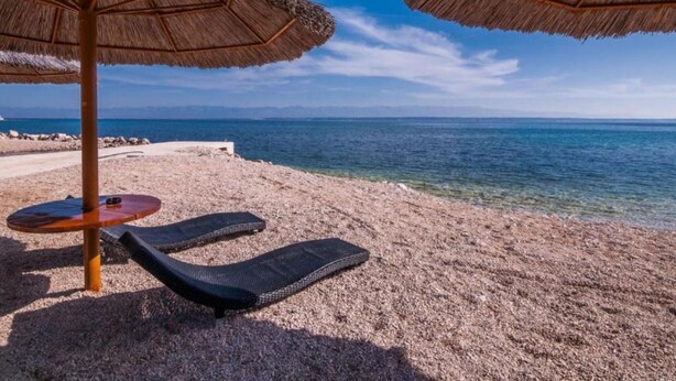 Ein Strand mit zwei Reetdachsonnenuren, einer Sandfläche und freiem Blick auf das Meer.