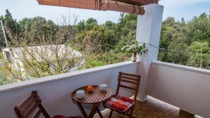 Ein Balkon mit zwei Holzstühlen, einem kleinen Tisch, einem Blumentopf und Blick auf Bäume und Gebäude.