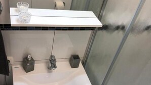 Un baño moderno con un lavamanos blanco, dos grifos y un vaso sobre la encimera.