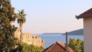 Vista costera con un antiguo fuerte de piedra, una palmera y un edificio con tejados de cerámica.