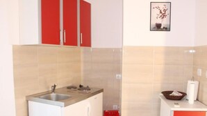 Cocina compacta con lavamanos, estufa y armarios rojos.